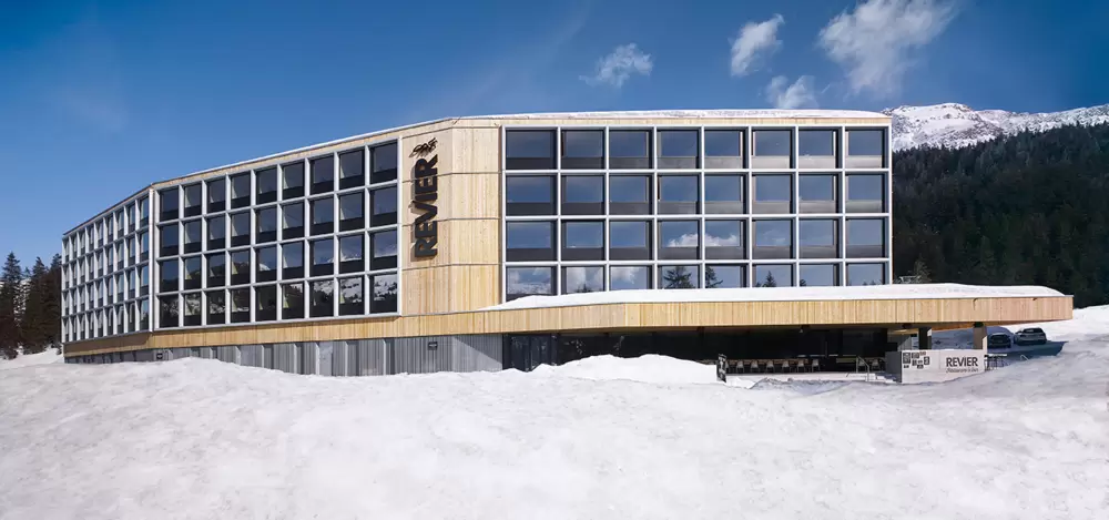 Hotelgebäude mit grosser Glasfassade vor schneebedeckten Bergen